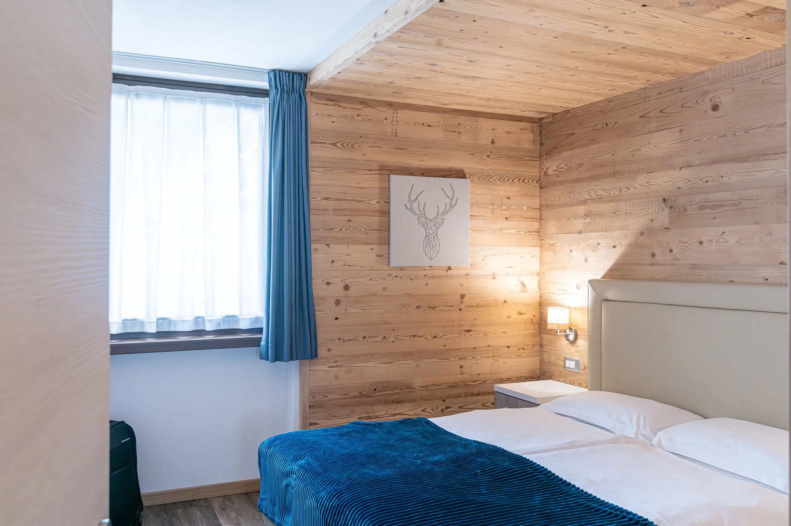 Camera in larice dell’Hotel Pedranzini, con la coperta blu e il quadro con il cervo