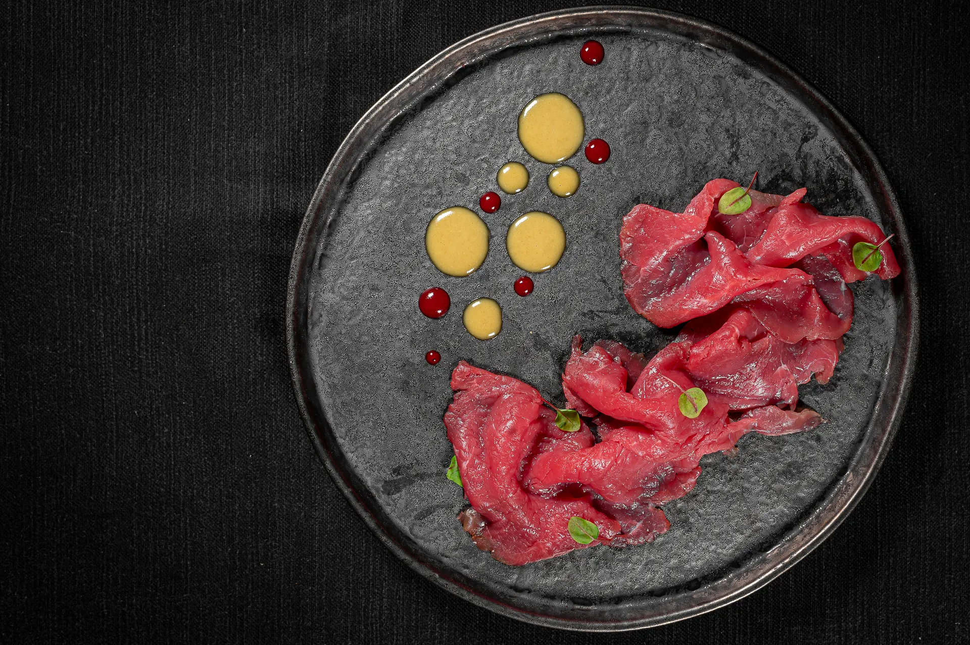 Carpaccio su piatto scuro, isolato su fondo nero