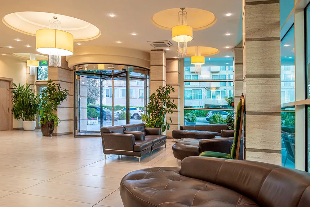 La hall dell’Hotel Adria con i divani in pelle e le vetrate sul verde
