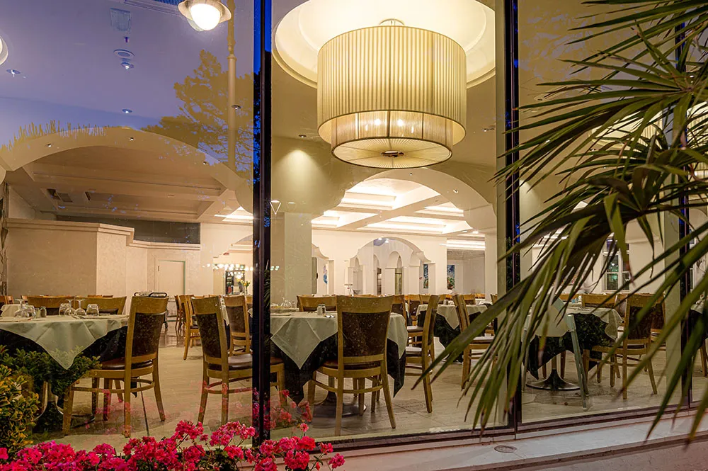 La sala ristorante vista dall’esterno all’ora blu, tra fiori e palme